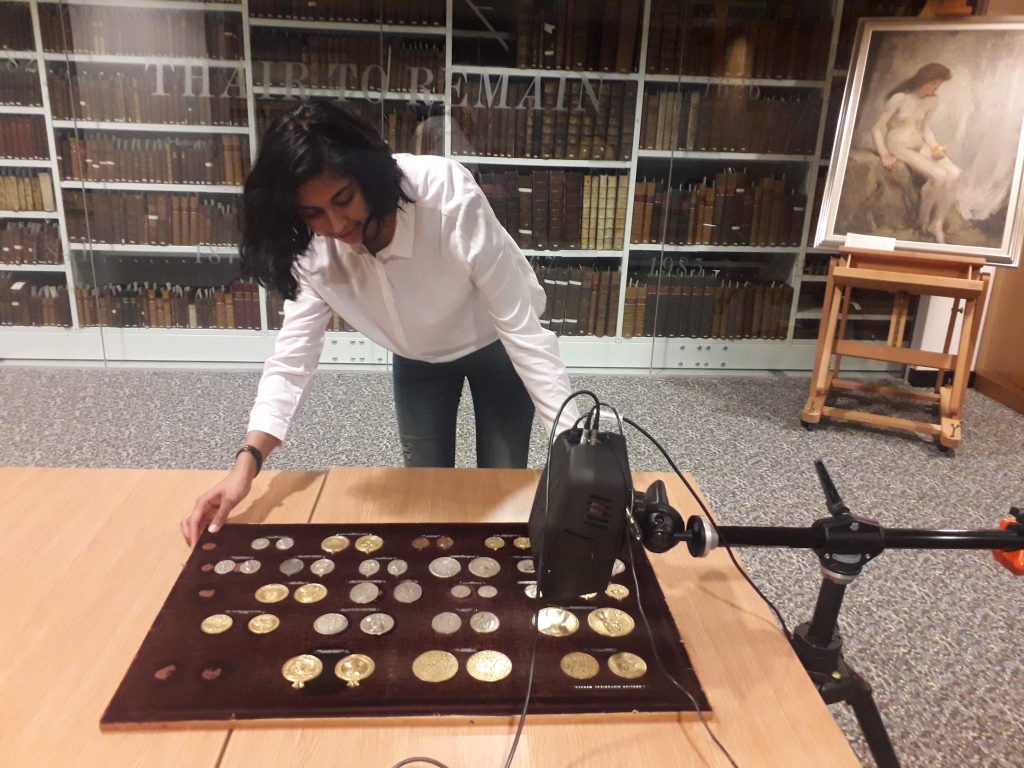 A woman using a large special black camera photography a plaque of coins.