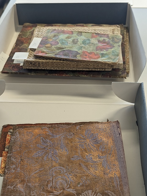 A box of small paperbound volumes with decorated paper wrappers. The volumes are messily piled on top of each other in a small box.