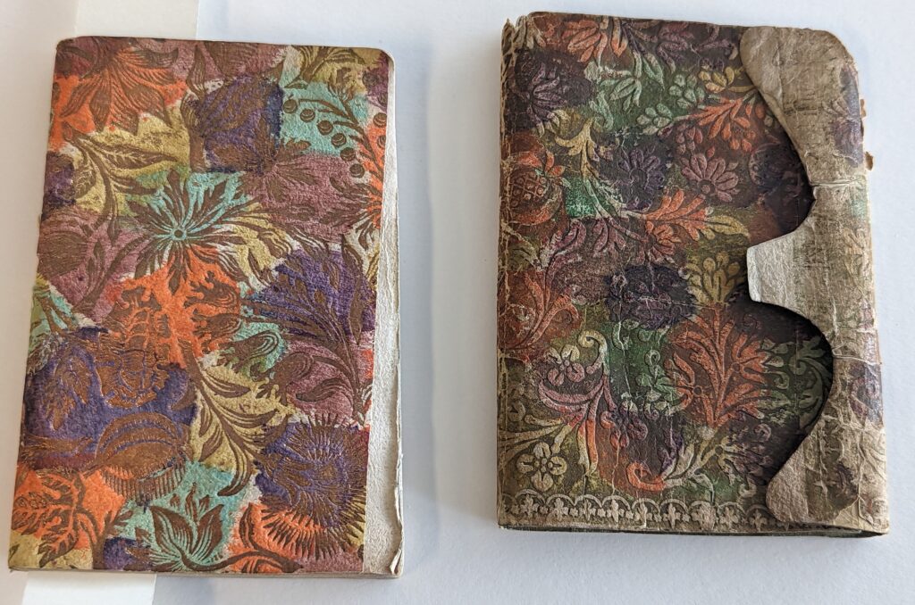 Image of a paper bound volume with a brocade paper wrapper. The paper paper has a gold background and swirling flower pattern with many different colours.