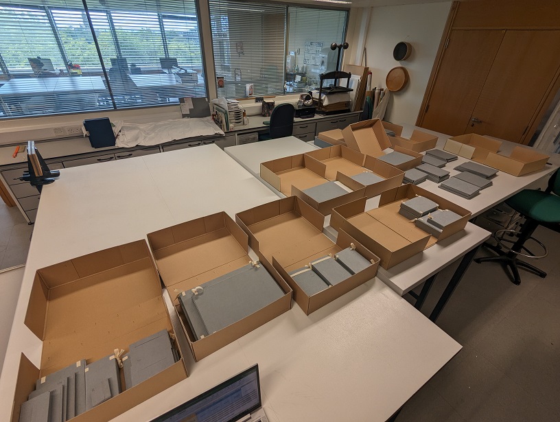 A large table is covered in boxes full of books that have been placed in custom made folders.